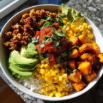 A vibrant sweet potato taco bowl featuring roasted sweet potatoes, seasoned ground filling, avocado, corn, salsa, and rice.