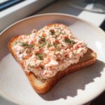 A slice of toasted bread generously topped with creamy smoked salmon dip and fresh dill.