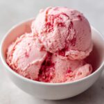Close-up of two scoops of pink, swirled strawberry ice cream served in a white bowl.