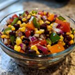 Close-up of a glass bowl filled with colorful Cowboy Caviar dip featuring black beans, corn, peppers, and red onion.