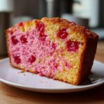 Close-up of a moist slice of vintage cherry cake showing yellow crumb marbled with bright pink and studded with glossy red cherries.