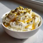 A bowl of creamy whipped feta dip drizzled with honey and sprinkled with chopped pistachios.