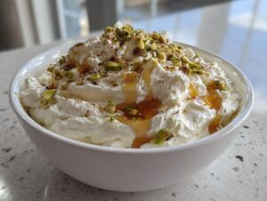 A white bowl filled with creamy whipped feta dip, drizzled with honey and topped with chopped pistachios.