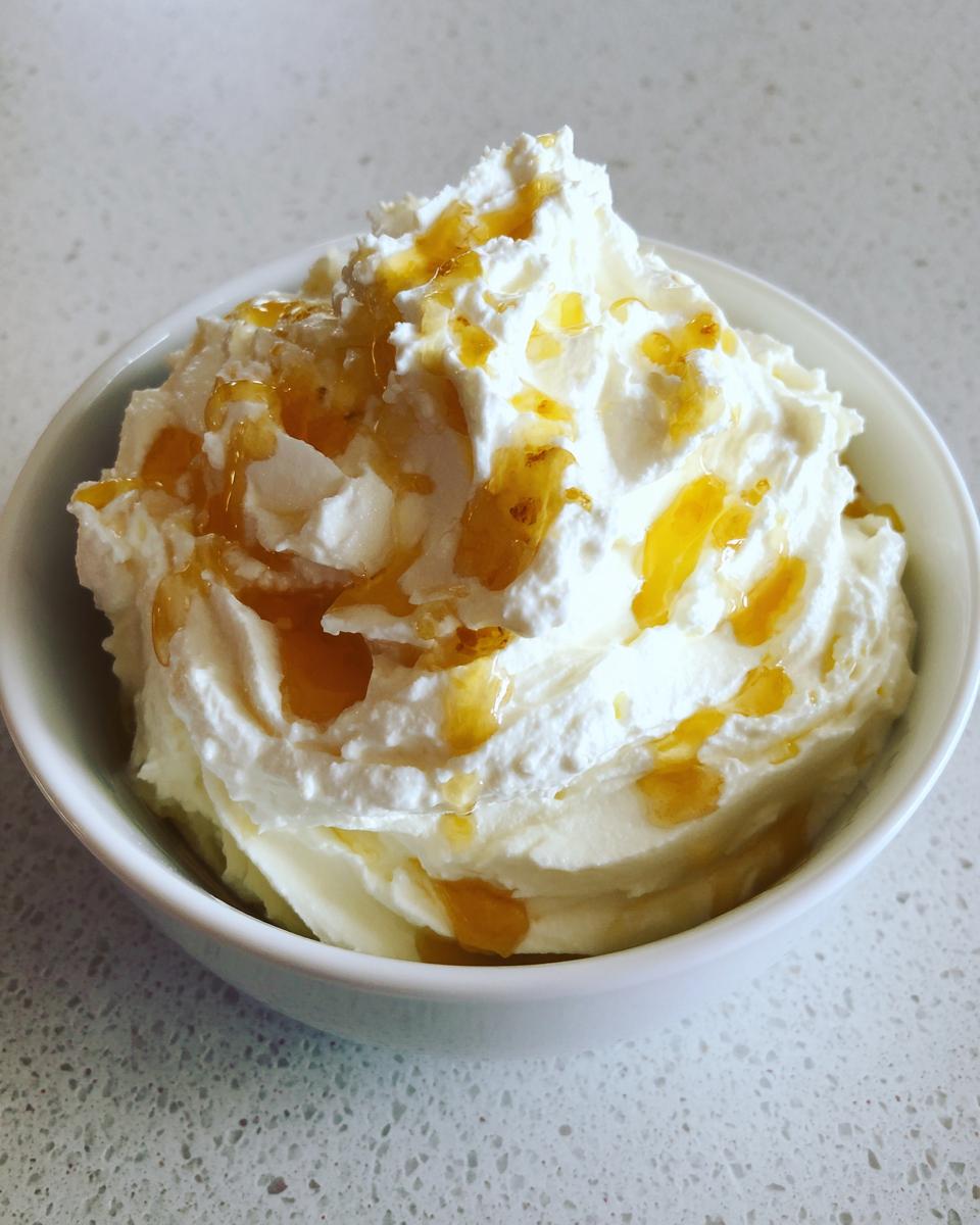 A bowl of light, fluffy whipped goat cheese topped with a generous drizzle of golden honey.