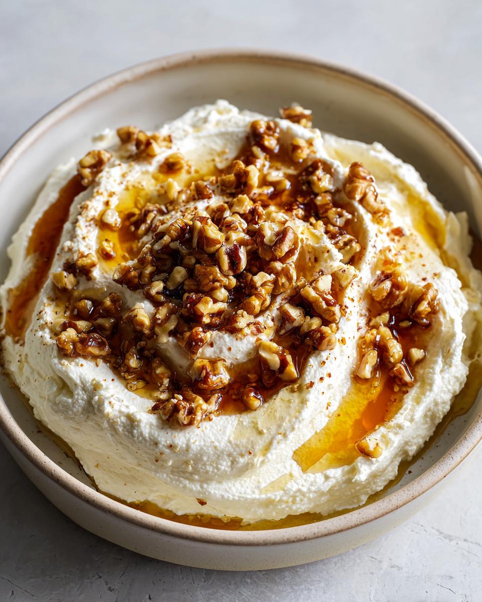 Close-up of creamy whipped ricotta dip topped generously with chopped walnuts and drizzled honey.