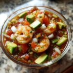 Close-up of a glass filled with vibrant mexican shrimp cocktail featuring plump shrimp, avocado chunks, and diced tomatoes.