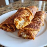 Close-up of rolled, fried tortillas filled with mashed potato mixture, resembling potato tacos.