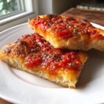Two slices of thick crust bread topped generously with vibrant red pizza sauce and herbs.