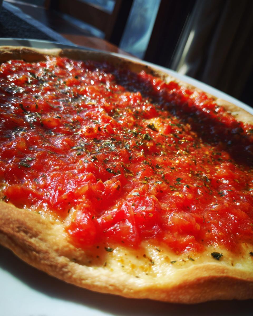 Close-up of a thick, bright red pizza sauce spread generously over dough, seasoned with herbs.