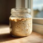 A highly active sourdough starter, full of bubbles and risen high in a clear glass jar.