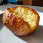 Close-up of a perfectly cooked air fryer baked potato, split open to show the fluffy interior and crispy, golden-brown skin.