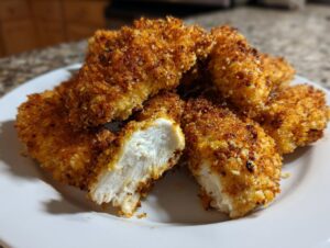 Close-up of golden brown, crispy air fryer chicken tenders, one cut open showing juicy white meat.
