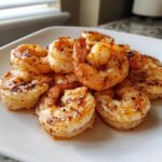 A close-up of seasoned and cooked air fryer frozen shrimp piled on a white plate.