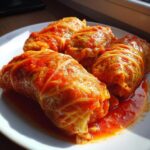 Four homemade cabbage rolls generously covered in a rich, bright red tomato sauce served on a white plate.