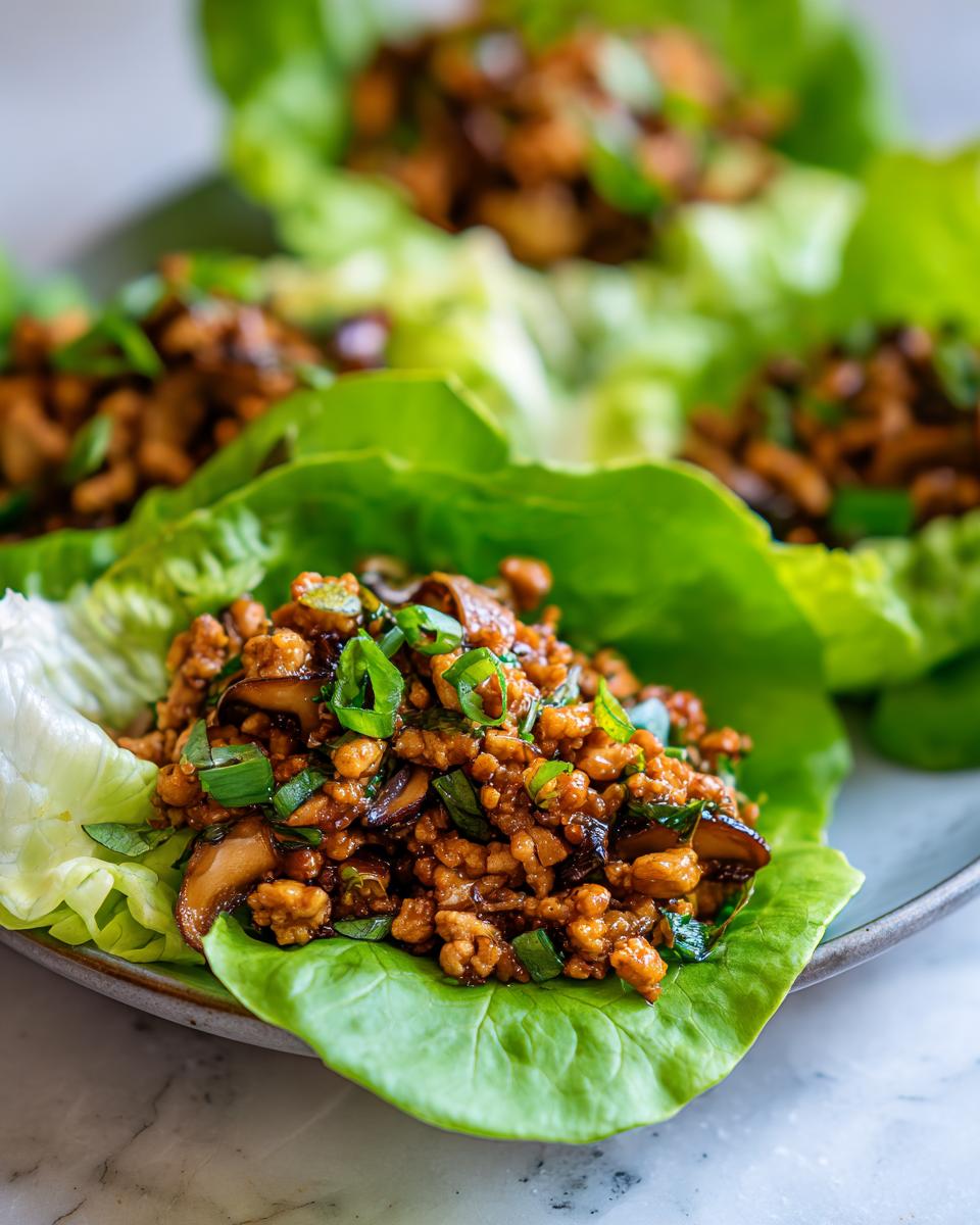 Close-up of savory chicken lettuce wraps filling with mushrooms and green onions in a crisp lettuce cup.