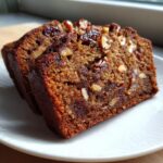 Two moist slices of date nut bread, rich brown in color, packed with visible dates and chopped nuts.
