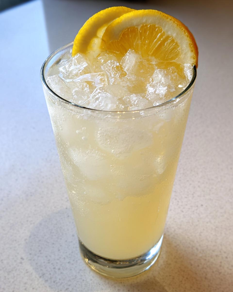 Tall glass filled with ice and refreshing lemonade, garnished with two thin slices of lemon on the rim.