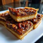 Three stacked squares of gooey pecan pie bars showing a thick shortbread crust and rich pecan topping.
