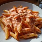 A close-up, appetizing shot of penne pasta coated in a creamy, orange-pink sauce and sprinkled with dried herbs, showcasing the amazing pink sauce pasta.