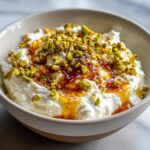 Close-up of a bowl of creamy ricotta dip drizzled with honey and topped with chopped green pistachios.