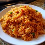 A close-up view of a mound of vibrant orange Spanish rice mixed with green peas served on a white plate.