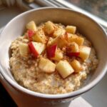 A creamy bowl of apple cinnamon oatmeal topped with diced red apples and a sprinkle of cinnamon.
