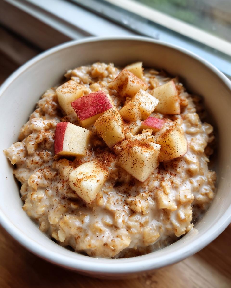 A close-up of a bowl of creamy apple cinnamon oatmeal topped with fresh diced apples and a sprinkle of cinnamon.