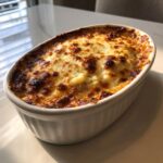 Oval white baking dish filled with hot caramelized onion dip, topped with bubbly, browned cheese.