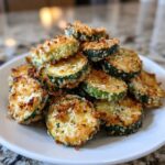 A pile of crispy, golden-brown baked parmesan zucchini slices stacked high on a white plate.