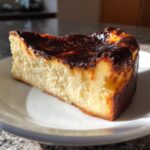 A rich, creamy slice of basque cheesecake showing its signature dark, caramelized top, served on a white plate.