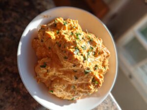 A close-up shot of a generous serving of bold, orange-hued remoulade sauce topped with fresh parsley in a white bowl.