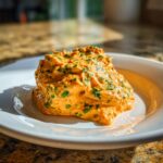 A dollop of vibrant orange remoulade sauce studded with green herbs served on a white plate.
