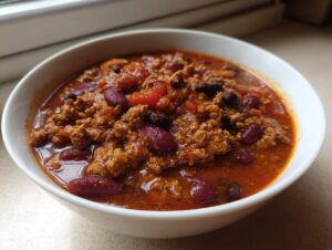A close-up of a white bowl filled with rich, hearty high protein chili featuring ground meat and kidney beans.