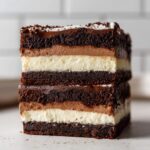 Close-up of a tall slice of brownie refrigerator cake showing five distinct layers: dark brownie, light mousse, white creamy layer, and repeating.