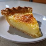 A close-up of a single slice of buttermilk pie showing the creamy yellow filling and golden-brown crust.