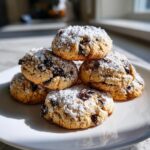A stack of freshly baked cannoli cookies, studded with chocolate chips and generously dusted with powdered sugar.
