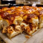 A close-up view of freshly baked bbq chicken sliders, showing shredded chicken, melted cheese, and a generous topping of BBQ sauce.