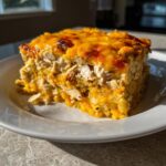 A square serving of cheesy chicken burrito bake with a golden-brown melted cheese top, sitting on a white plate.