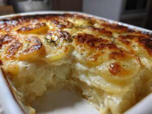 Close-up of creamy, cheesy scalloped potatoes with a browned, bubbly top garnished with thyme.