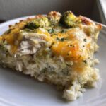 Close-up of a cheesy slice of chicken cauliflower rice casserole topped with broccoli florets and parsley.