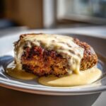 A perfectly cooked piece of chicken fried steak smothered in creamy white gravy, served on a white plate.