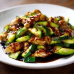A close-up of glistening chicken zucchini stir fry coated in a dark, savory sauce, served on a white plate.