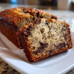 Close-up of sliced vegan banana bread studded with chocolate chips on a white plate.