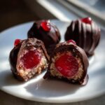 Close-up of chocolate covered cherries, one cut in half revealing the bright red cherry center and creamy filling.