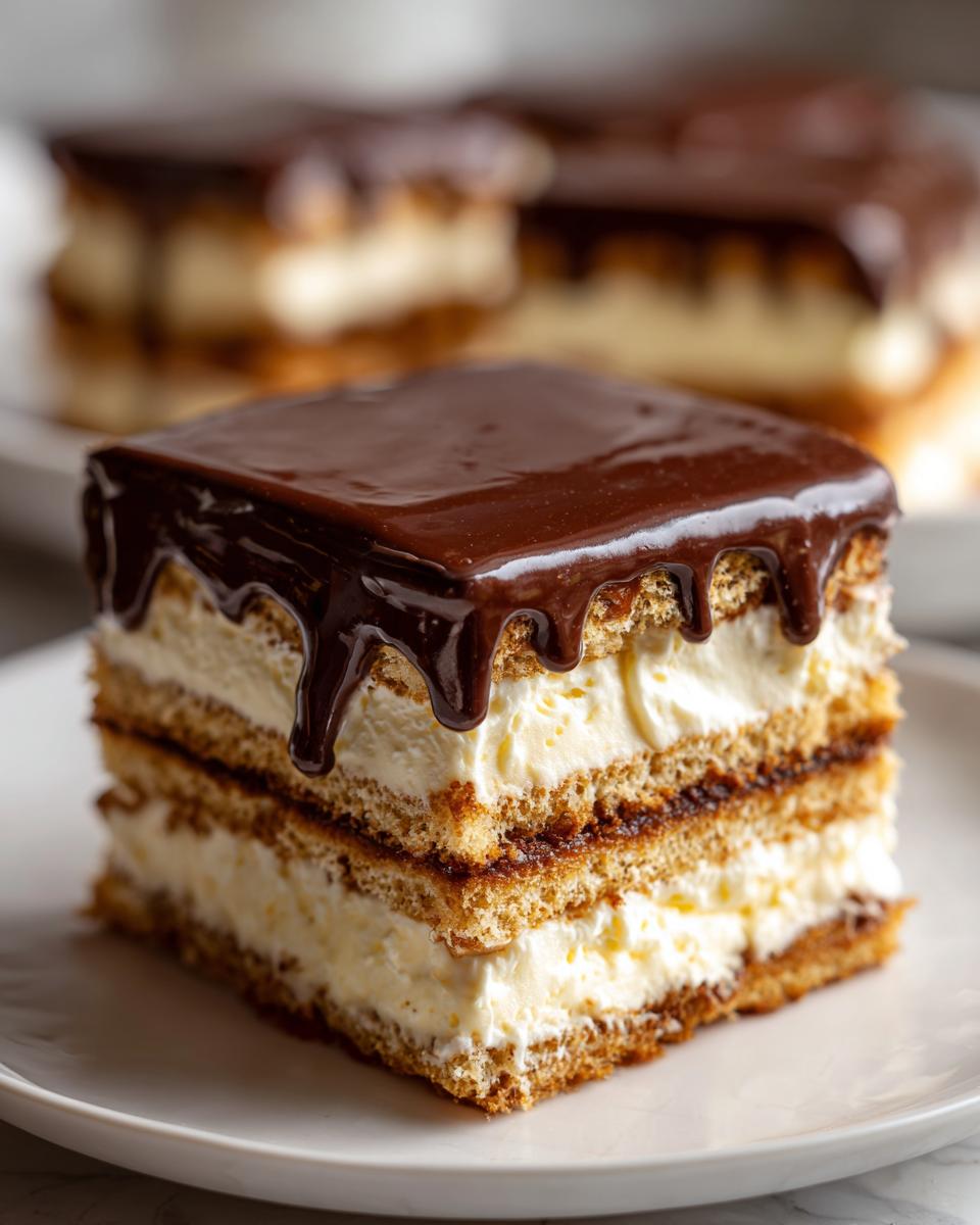 A decadent slice of chocolate eclair cake featuring layers of graham cracker, cream filling, and rich chocolate ganache topping.