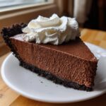 A decadent slice of chocolate mousse pie featuring a dark crust, thick chocolate filling, and topped with a swirl of whipped cream.