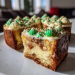 A slice of rich Christmas tree cheesecake topped with white frosting, green piped trees, and festive sprinkles.