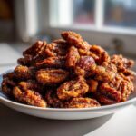 A close-up of a white bowl piled high with glistening, candied cinnamon sugar pecans catching the sunlight.