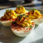 Four halves of classic deviled eggs, filled with piped yolk mixture, sprinkled with paprika and chives.