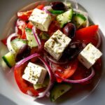 Vibrant close-up of a fresh greek salad featuring large cubes of feta cheese, red tomatoes, cucumber, red onion, and Kalamata olives.